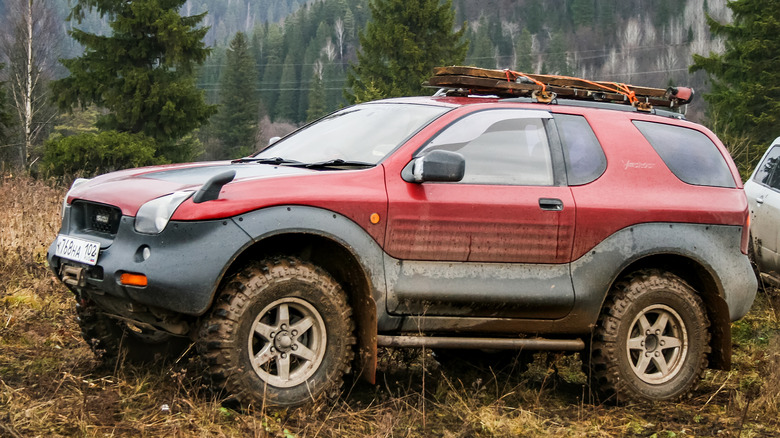 A muddy, red Isuzu VehiCross parked in a field