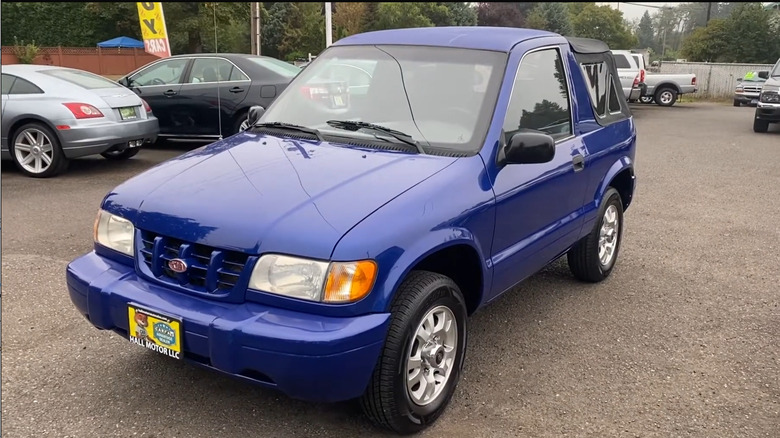 A blue 2000 Kia Sportage Convertible in a used car dealership parking lot