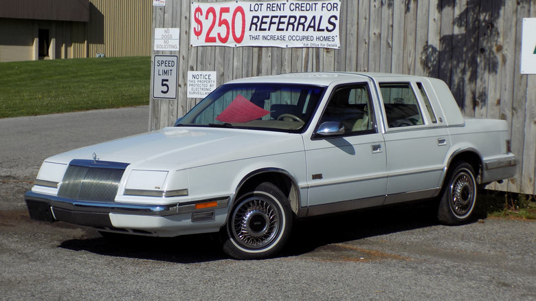 White Chrysler Imperial parked in front of a wooden fence