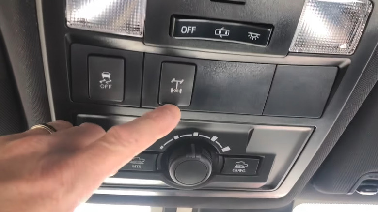 A man's left index finger pointing to the center locking differential button mounted to the roof console of his SUV.
