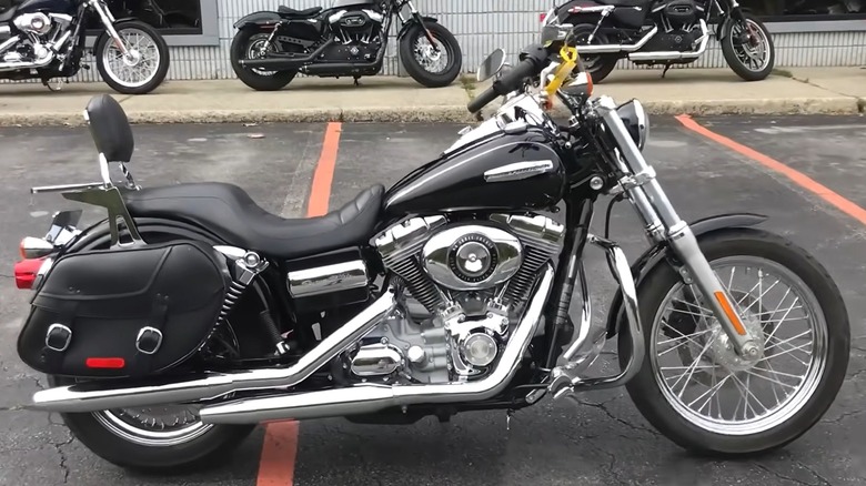 A black Harley-Davidson cruiser parked in a dealership lot, equipped with leather saddlebags and chrome accents.