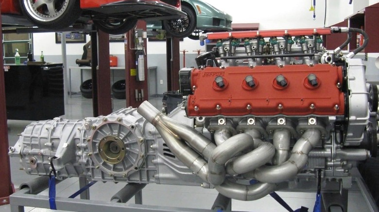 A Bimota V-Due 500 engine mounted on a stand in a workshop, showcasing its red valve covers, intricate headers, and attached transmission.