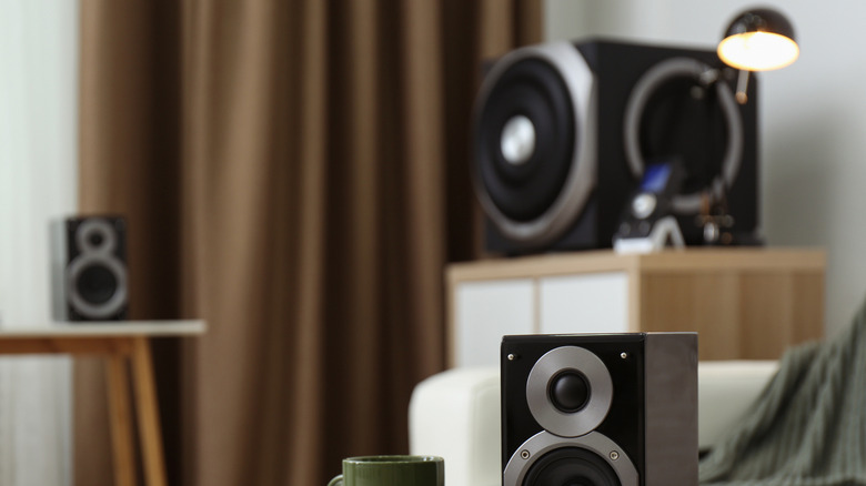 A speaker on top of a table with the subwoofer beside the sofa