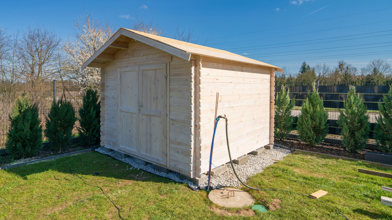 An exterior view of enclosed wooden shed with greenery and blue skies in the background.