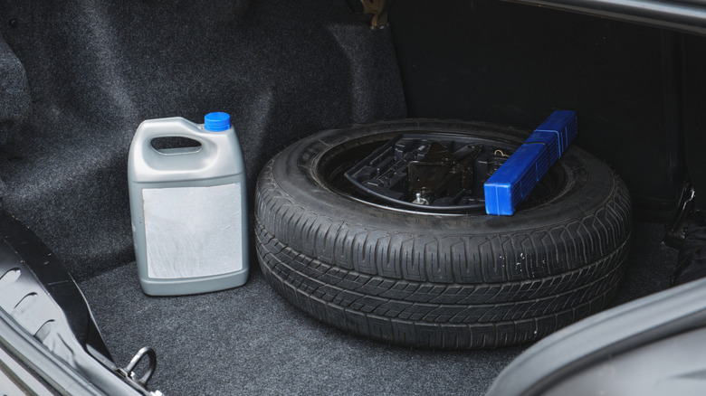 A car's trunk with a spare tire, a blue triangle cover, and a gray canister with a blue cap