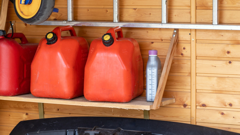 Three red jerry cans with yellow lids placed onto a wooden wall shelf