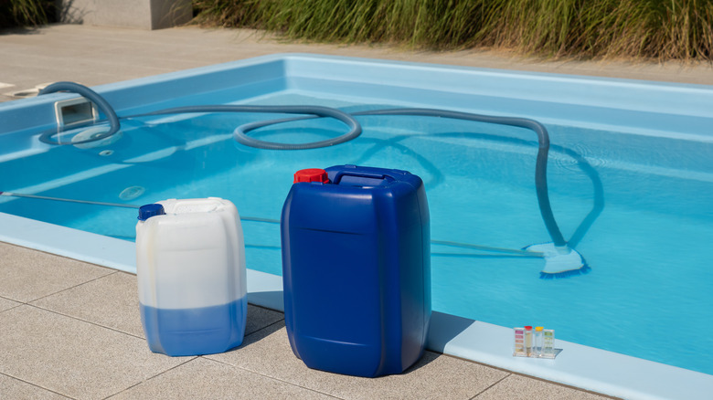Pool chemicals in front of a pool filled with water and a long hose.