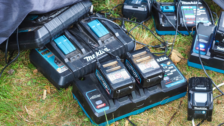 A collection of Makita batteries and chargers lying on a lawn