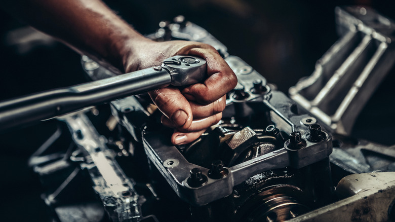 A person's hand using a wrench on an engine.