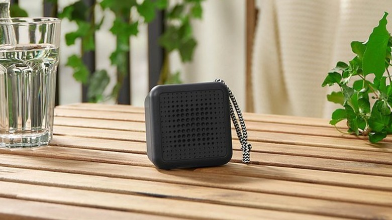 An Ikea Vappeby wireless speaker on a table next to a glass