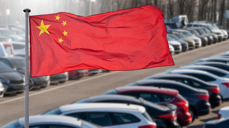 The red Chinese national flag against a background of newly made cars sitting in a lot