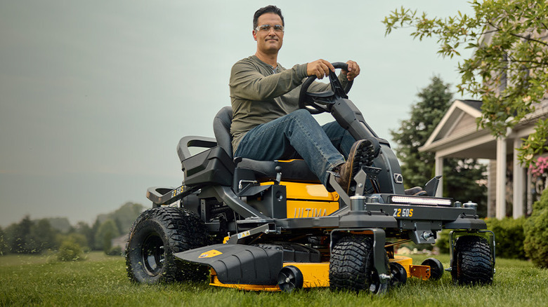 Person riding an Ultima Series Cub Cadet lawn mower on grass with a house in the background
