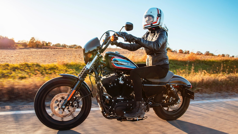 A rider in full leather kit with helmet riding a 2021 Harley Sportster 1200 Iron down a road