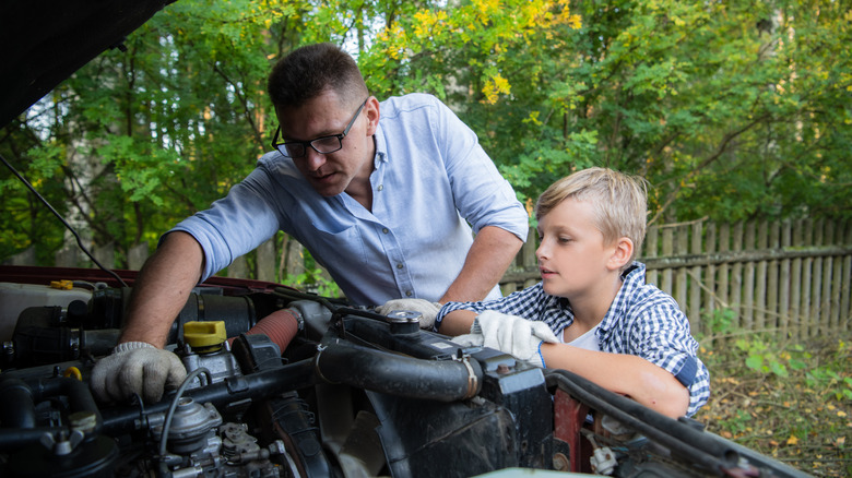 A man showing a young boy how to work on something under the hood of a vehicle