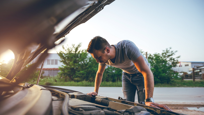 A young man carefully inspecting underneath his car's hood