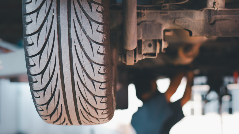 A mechanic working underneath a vehicle with a tire in the foreground