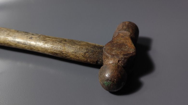 An antique ball peen hammer on a gray surface.