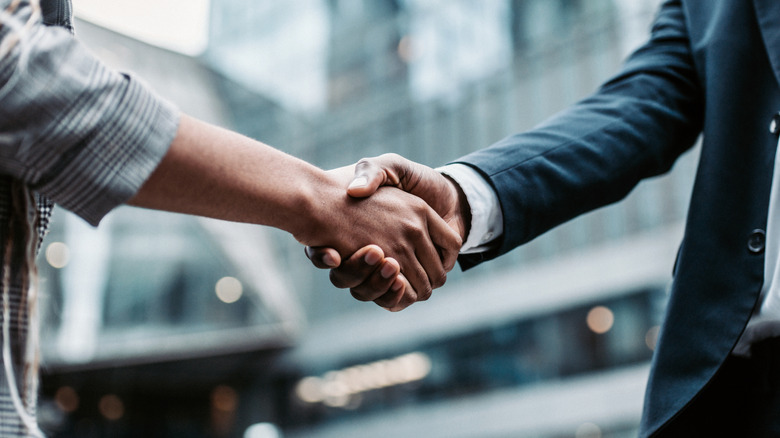 Two people shaking hands before a blurry city backdrop.