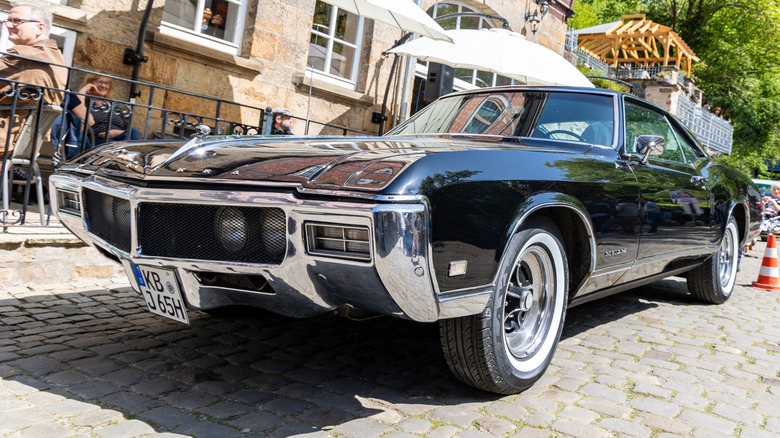 The front-left view of a Black Buick Riviera parked in front of a house