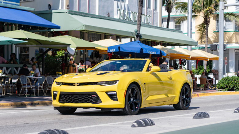 A yellow and black Chevrolet Camaro moving down a street.