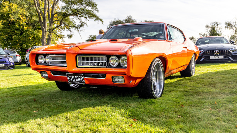 An orange Pontiac GTO parked in a field, front-left view visible