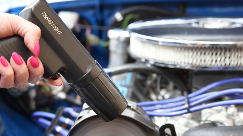 A hand holding a timing light over an engine.