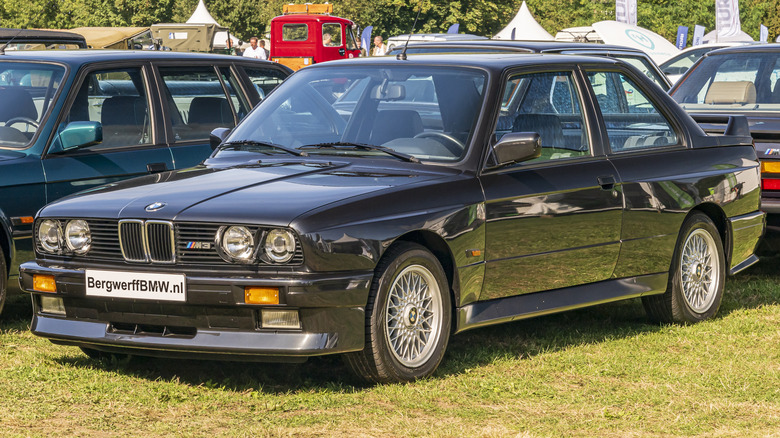 Front 3/4 view of black BMW E30 M3 parked at car show.