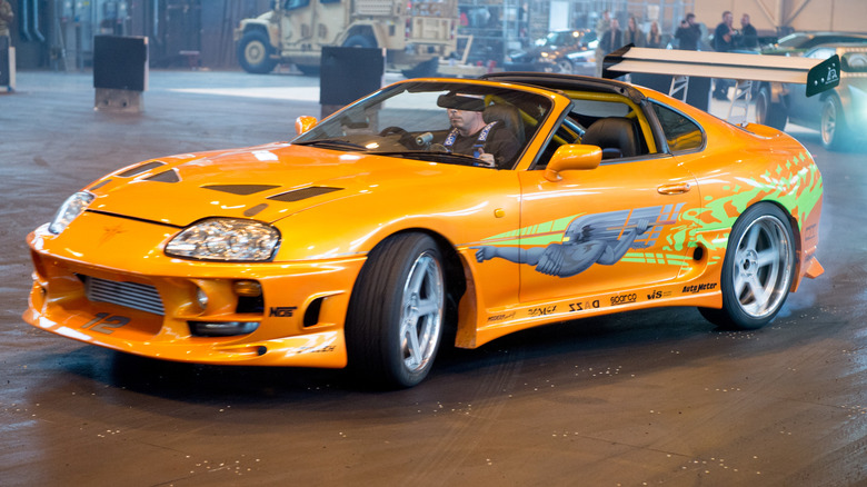 Close-up view of Orange Fast and Furious Toyota Supra doing donuts at car show.