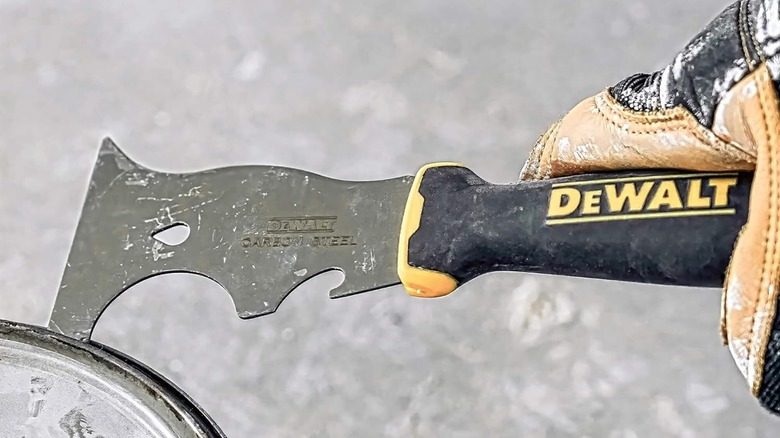 A person opening paint can with tool