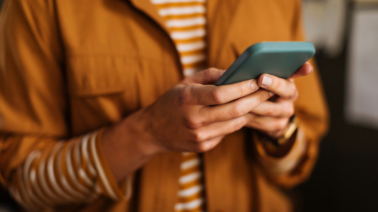 close-up of person waring burnt orange using a smartphone
