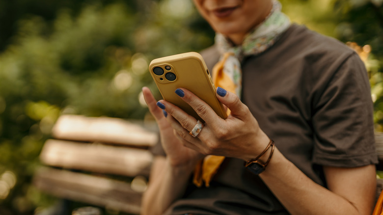 close-up of a woman holding a smartphone while sitting on a park bench