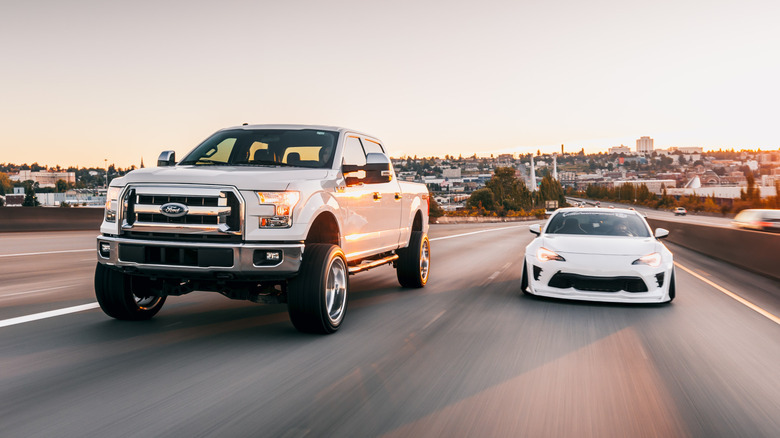 A white Ford pickup truck driving next to a white sports car on a highway