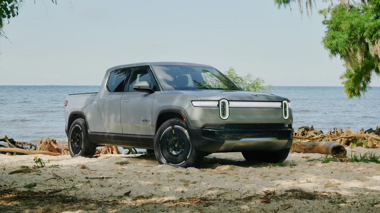 Front 3/4 view of a silver Rivian R1T parked on a beach, front 3/4 view