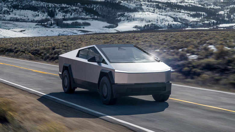 A Tesla Cybertruck on a paved road with snow hills in the background, front 3/4 view, higher angle