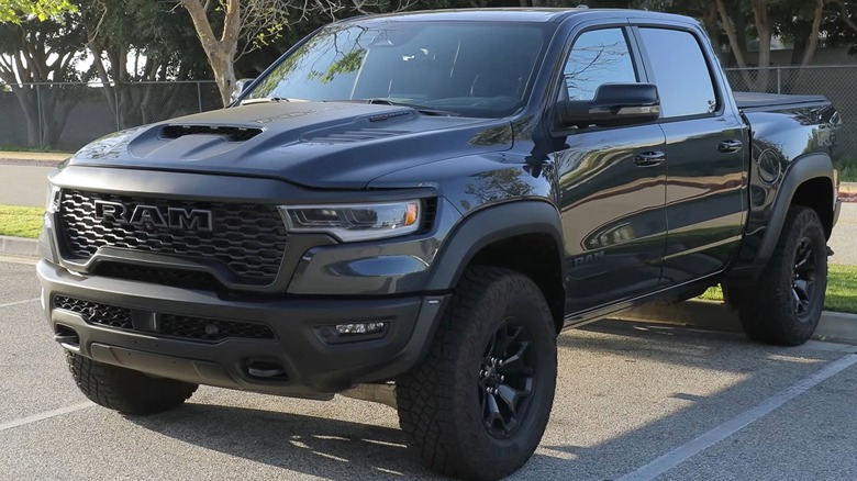 A dark gray 2025 Ram 1500 TRX parked in front of trees in a lot.