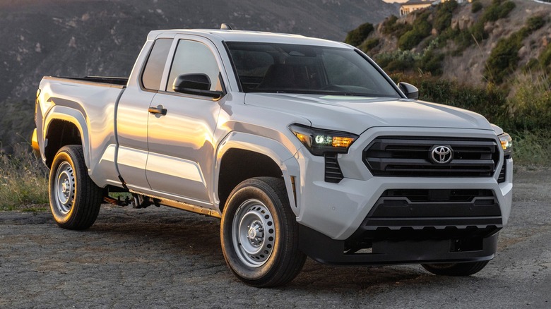 A white 2025 Toyota Tacoma SR parked on a dusty hillside with mountains stretching out in the background.