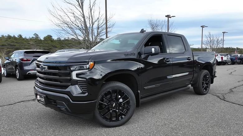 A 2025 black Chevrolet Silverado 1500 High country is surrounded by other vehicles, with a cloudy sky overhead giving it this showroom-style vibe.