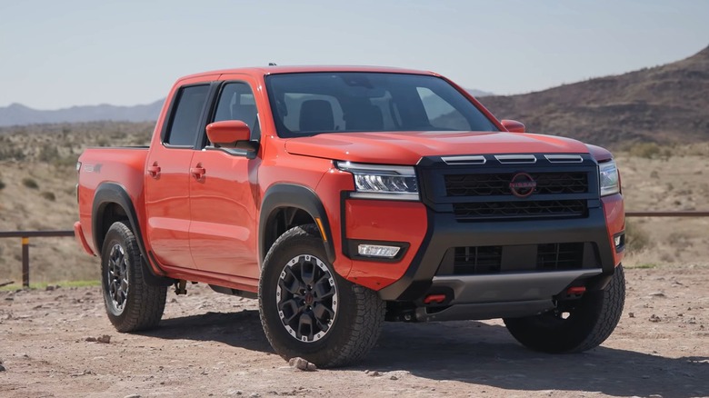 A bright orange 2025 Nissan Frontier Pro-4x looking ready for off-road use in a dry desert landscape with mountains in the background.
