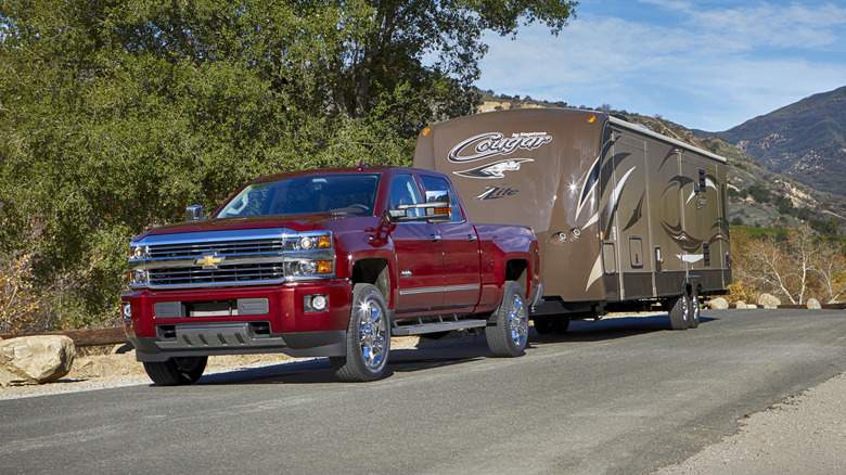 A red 2015 Chevrolet Silverado pulling a trailer on a public road.