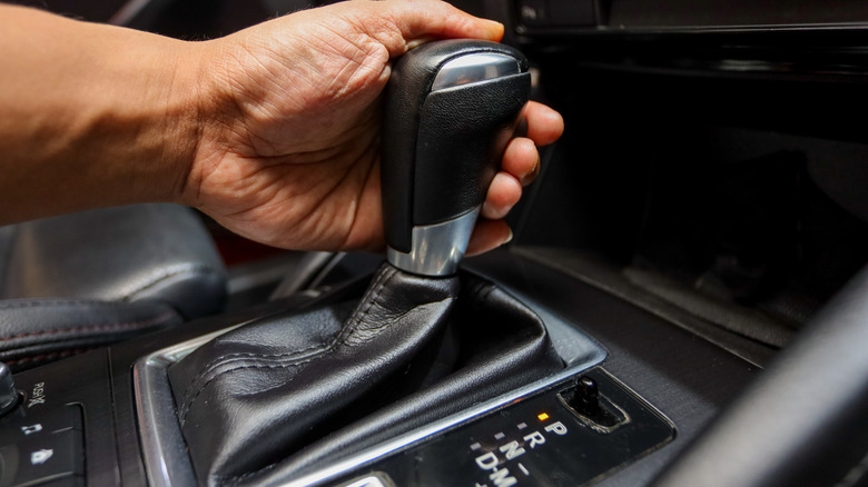 A person holding an automatic transmission lever.