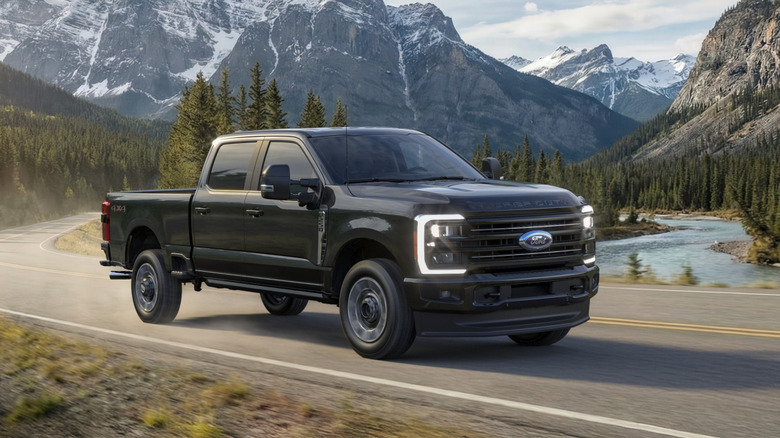 Front 3/4 view black Ford Super Duty truck driving on mountain highway.