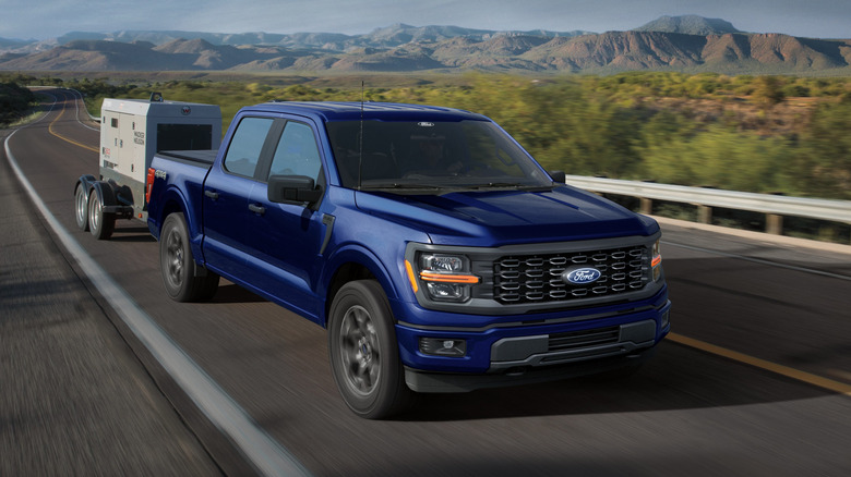 Front 3/4 view of blue Ford F-150 towing trailer on desert highway.