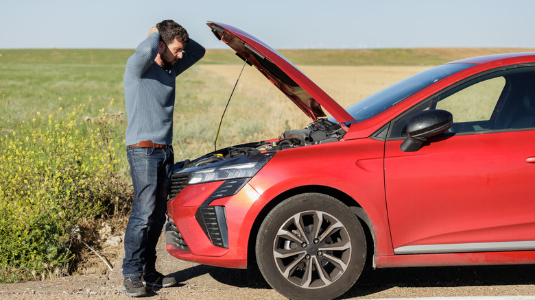 man looking at broken down car with hood up