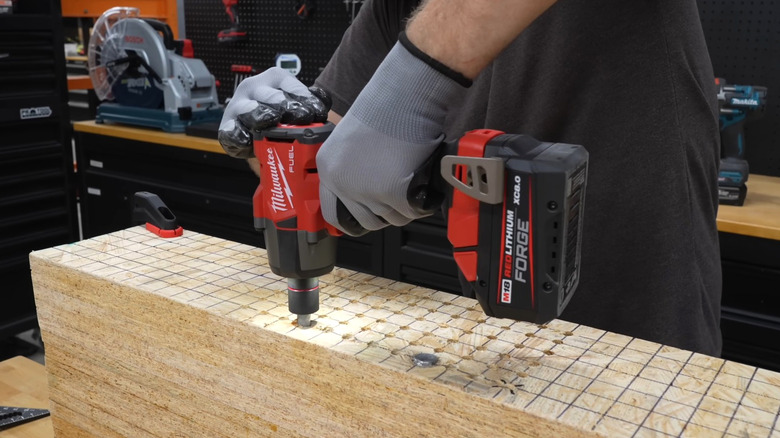Person using Milwaukee red and black impact wrench on lumber.