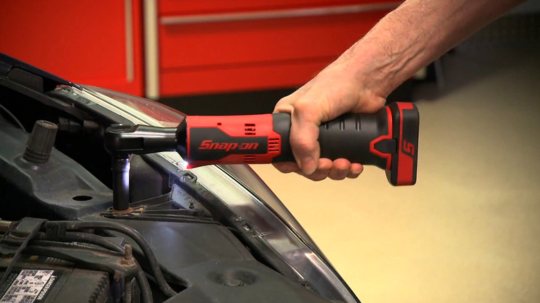 A Snap-On red and black cordless ratcheting wrench used to remove engine fasteners.