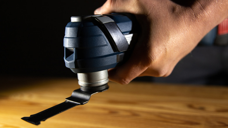 A person holding an oscillating multi-tool above a wooden bench