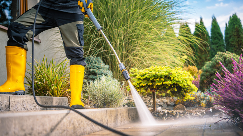 person using pressure washer on stone walkway