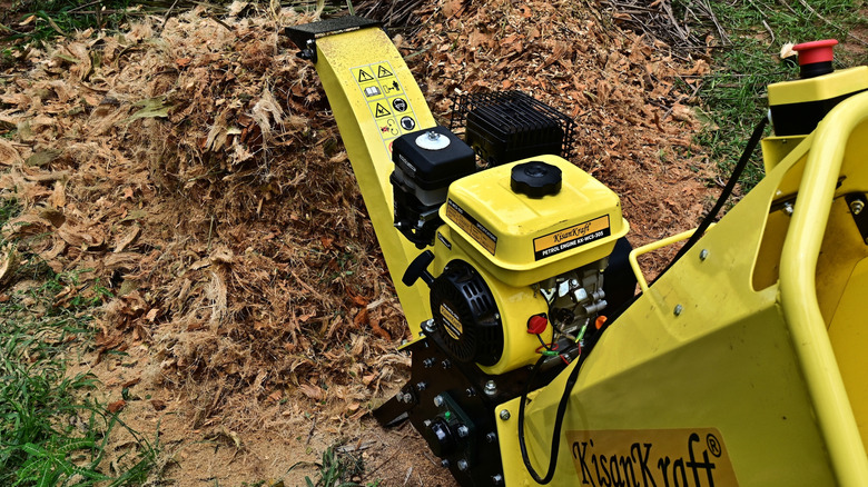 yellow wood chipper next to wood chip pile