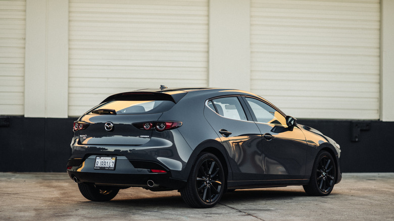 Black 2026 Mazda3 hatchback with available six-speed manual parked in front of a white and black wall.