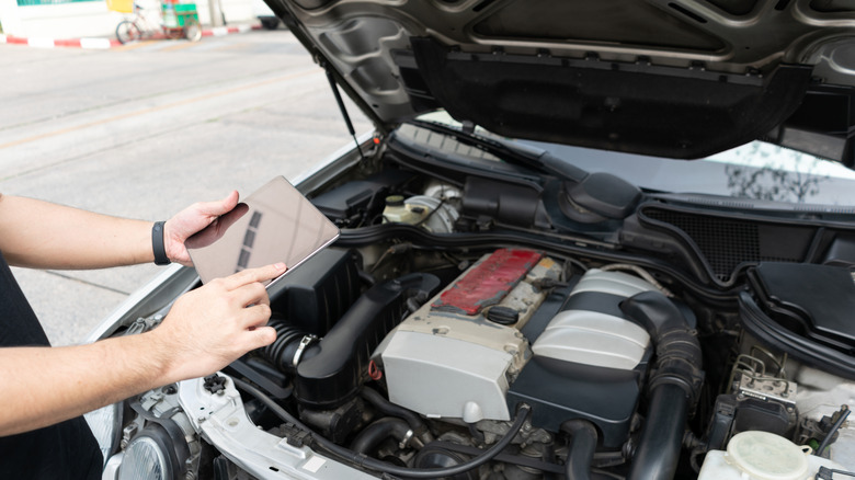 Mechanic holding tablet over engine of a 2000s Mercedes-Benz
